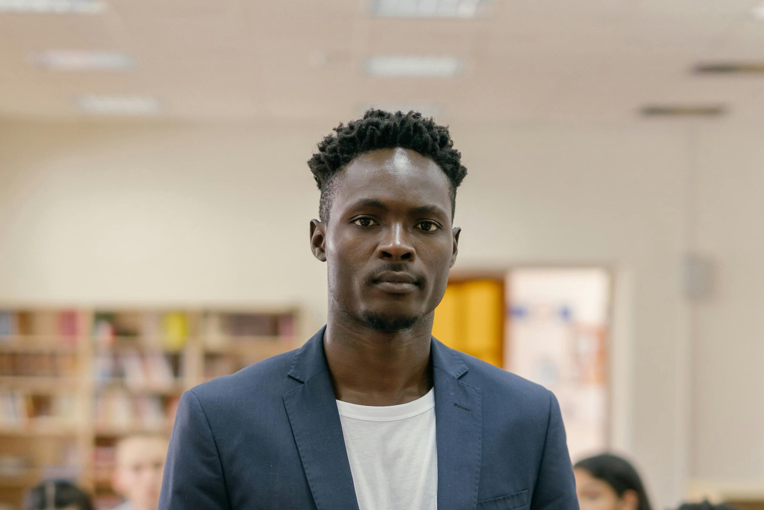 pexels-photo-9159050-9159050 A student stands confidently in a college library surrounded by peers working on laptops.
